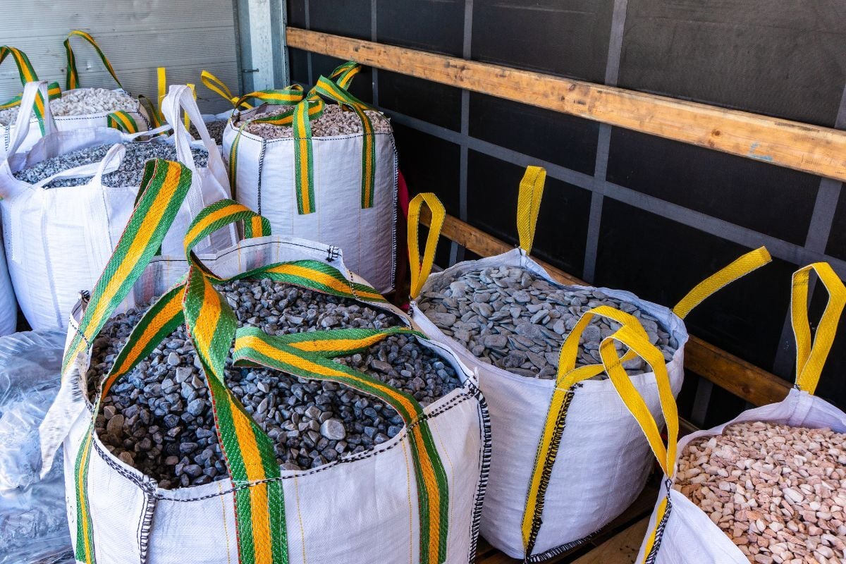 Several white bulk bags containing various types of aggregates, such as gravel and crushed stone, placed inside the cargo area of a truck