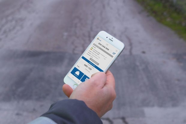 Smartphone in a person’s hand displaying an mScales weighing code, with an outdoor background of a yard or road surface