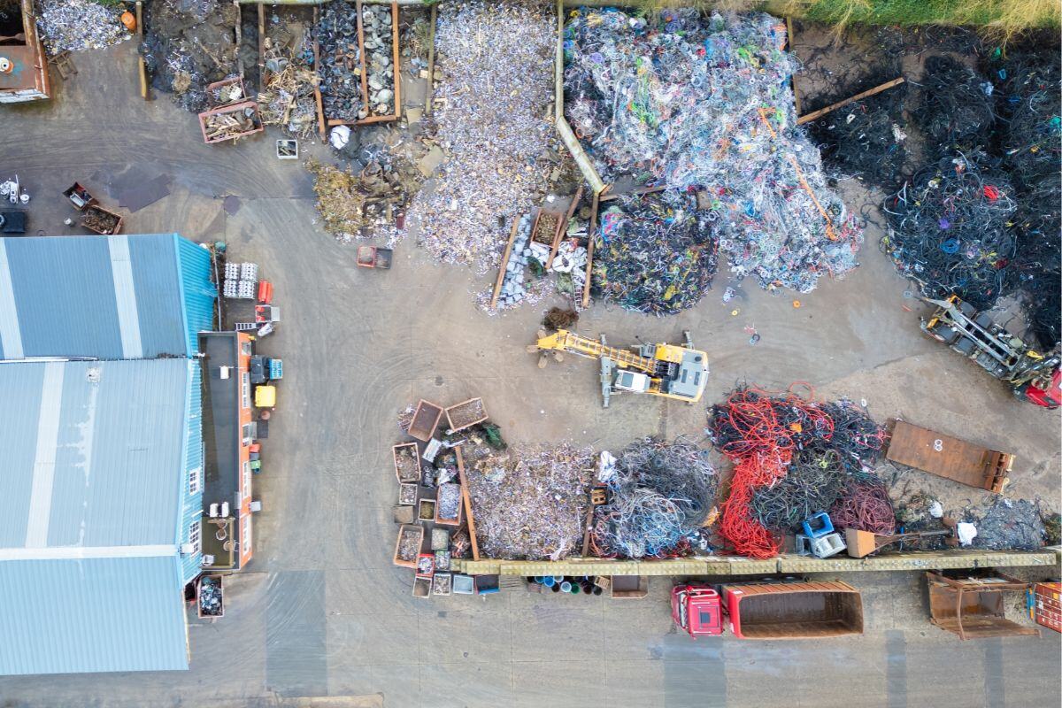 Aerial view of a recycling or scrap yard with piles of sorted materials like metal, plastic, and wires, along with containers, crates, and machinery used for processing and handling.